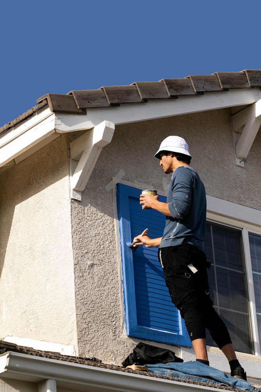 Painter on a ladder brushing paint onto a window shutter
